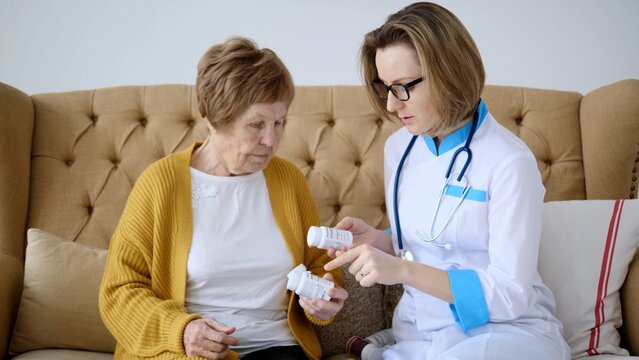 Female doctor is sitting next to an elderly woman on a sofa, carefully explaining the prescription and dosage of medicine, ensuring the patient's understanding and adherence to the treatment plan