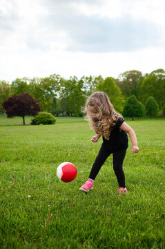 Happy little girl long blonde curls kicking pink soccer ball in