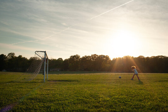 Side view tween girl kicking soccer ball into net sunny field