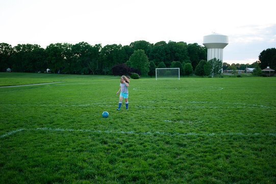 Young girl blonde hair kicking soccer ball on green field