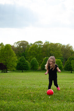 Little girl long blonde curls running with pink soccer ball in g