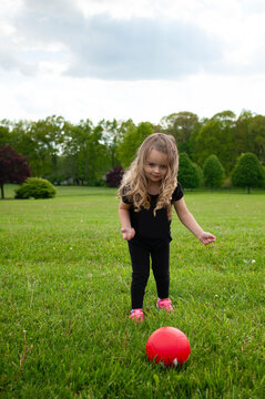 Little girl long blonde hair kicking pink soccer ball in green f