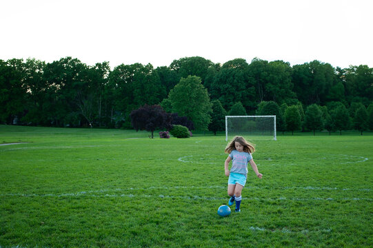 Young girl dribbling soccer ball during practice on green field