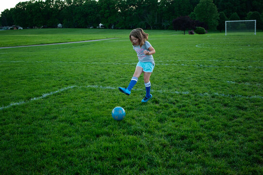 Young girl kicking soccer ball on green field