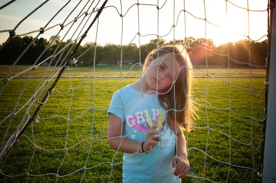 Up close young girl looking through soccer goal net green field