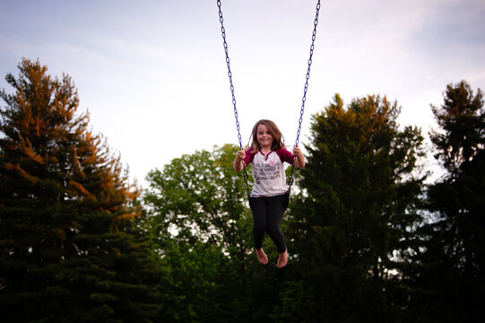 Happy tween girl playing on swings at school playground