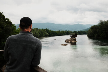 Man in a grey fleece jacket looking at the iconic house on the Drina River from a wooden viewpoint. Rear view. A popular tourist destination. Serbia country in spring season.