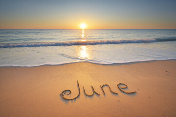 June word written on the sandy sea coast shore.