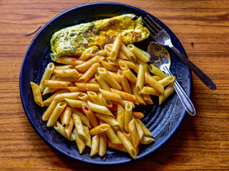 A plate of penne pasta and a cooked egg on a wooden table.