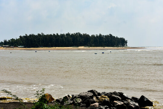 A serene coastal landscape with calm water, rocks, and a dense forest line near Digha. 