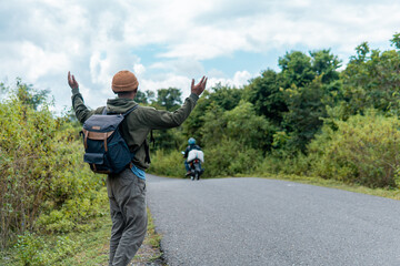 Indonesian traveler stands on a rural road, arms raised in frustration as a motorcycle passes...