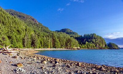 Porteau Cove Provincial Park. Sunny summer day. Sea and mountains, beach in foreground, mountain range in background against clear blue sky. British Columbia