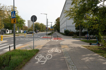 A view of a modern city street in Warsaw with organized traffic flow. A dedicated bicycle lane and sidewalk run parallel to the multi-lane road with clear signage.