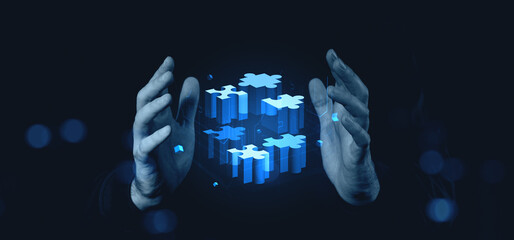 Hands holding digital puzzle blocks in blue glow on dark background conceptually..