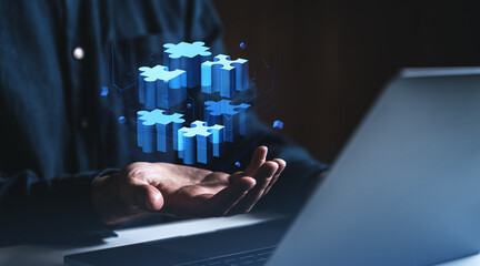 Businessman holding digital puzzle blocks above hand near laptop in dark room.