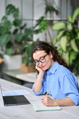 Busy young business woman using laptop writing notes. Female employee having remote virtual work conference meeting call in office or watching webcast online webinar training course, vertical.