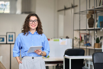 Happy confident 30s female company worker sales manager holding digital tablet standing in modern...
