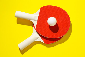 Ping pong rackets and ball on yellow background, top view