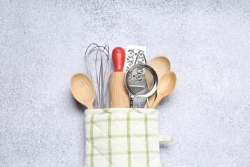 Different kitchen utensils in oven mitten on light table, top view