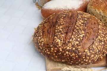 Fresh bread loaves and spikes on white tiled table, closeup