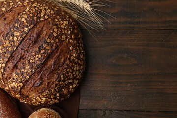 Freshly baked loaves of bread and spikes on wooden table, flat lay. Space for text