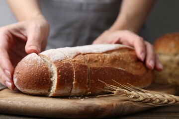 Woman with freshly baked bread at wooden table against grey background, closeup