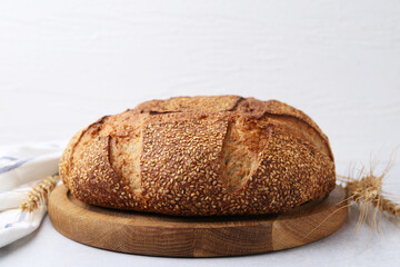 Freshly baked bread with sesame seeds and spikes on grey table against light background, closeup