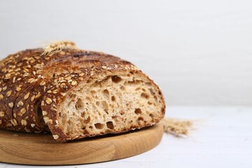 Freshly baked loaf of bread with oat flakes on light table, closeup. Space for text