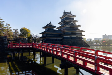 Matsumoto Castle viewed from a red wooden bridge, bathed in soft morning light with reflections in the calm moat water