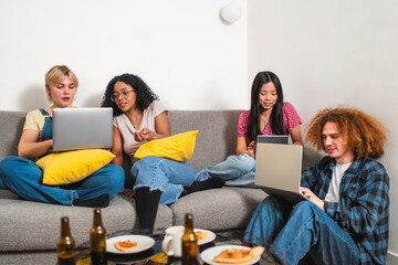 Four young multiethnic university students working and studying together at home, sitting on a grey...