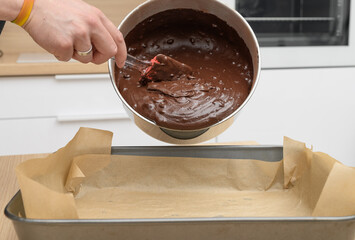 The chef transfers the raw chocolate dough to a baking tin lined with baking paper.