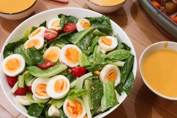 close up of homemade salad of boiled egg cut in slices, cherry tomato, lettuce in a big white bowl  with pumpkin cream soup in the side