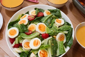 close up of homemade salad of boiled egg cut in slices, cherry tomato, lettuce in a big white bowl  with pumpkin cream soup in the side