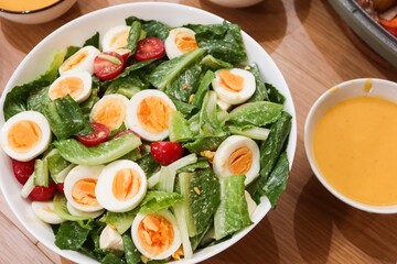 close up of homemade salad of boiled egg cut in slices, cherry tomato, lettuce in a big white bowl  with pumpkin cream soup in the side