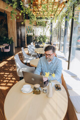 Senior businessman working on laptop in modern cafe, enjoying a cup of tea