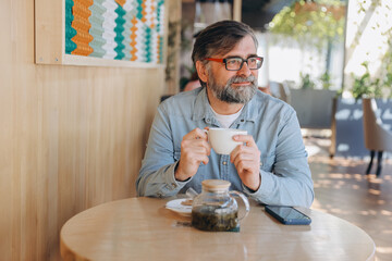 Senior Man Enjoying a Cup of Tea in a Modern Cafe