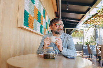 Senior man drinking tea in modern cafe looking away