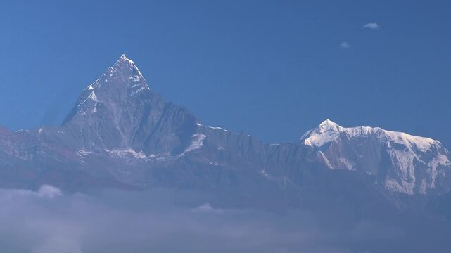 Timelapse capturing the iconic fishtail peak of Mt. Machapuchare alongside the Annapurna range under a glowing morning sky. Wisps of clouds drift below.