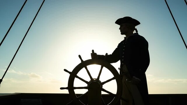 Silhouette of captain steering vintage sailing ship at sunset against clear sky
