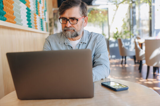 Senior businessman working on laptop in cafe - Powered by Adobe