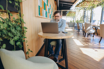 Senior businessman working on laptop in modern cafe