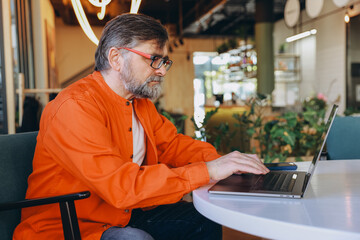 Senior Man Working on Laptop in Modern Cafe