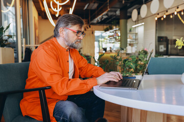 Senior Man Working on Laptop in Modern Cafe