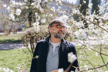 Senior man suffering from allergy symptoms near blooming tree in spring