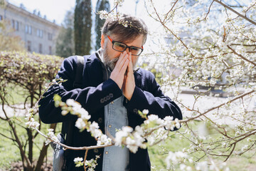 Senior man suffering from pollen allergy near blooming tree