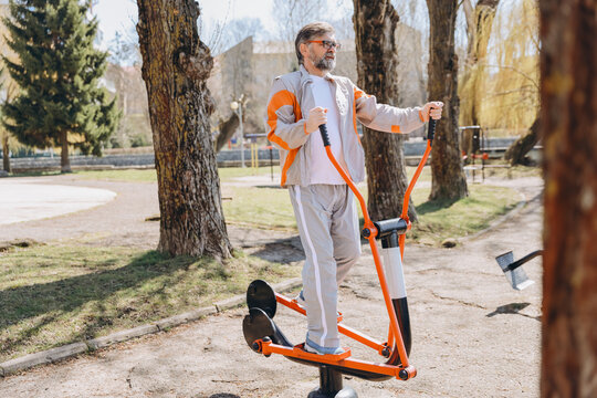 Senior man exercising on elliptical trainer in outdoor gym - Powered by Adobe