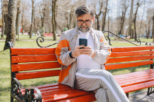 Senior man using smartphone sitting on bench in park