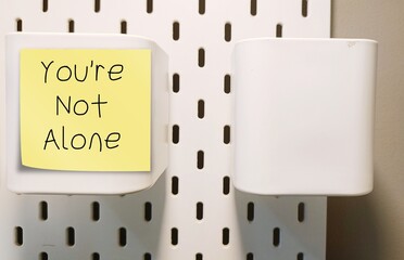 Stick note written YOU'RE NOT ALONE - positive self talk affirmation, encouragement message to...