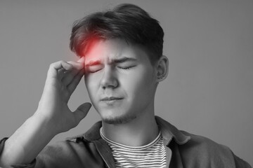 Young man suffering from headache on grey background