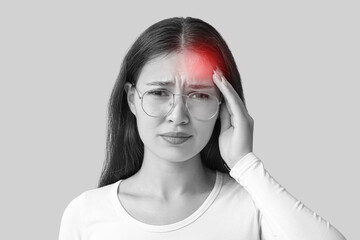Young Asian woman suffering from headache on grey background. Brain Injury Awareness Month